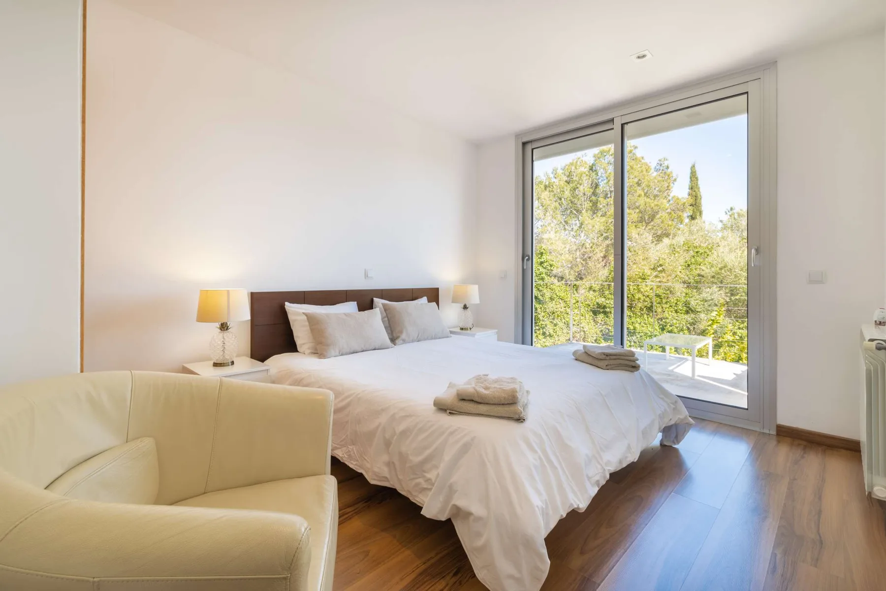 A bright bedroom with a neatly made bed and large glass doors opening to greenery.