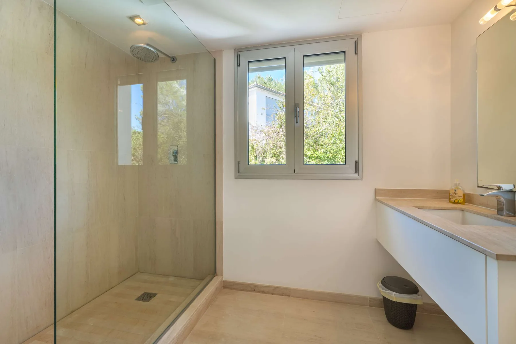 A bathroom with a glass shower, a window, and a long vanity.