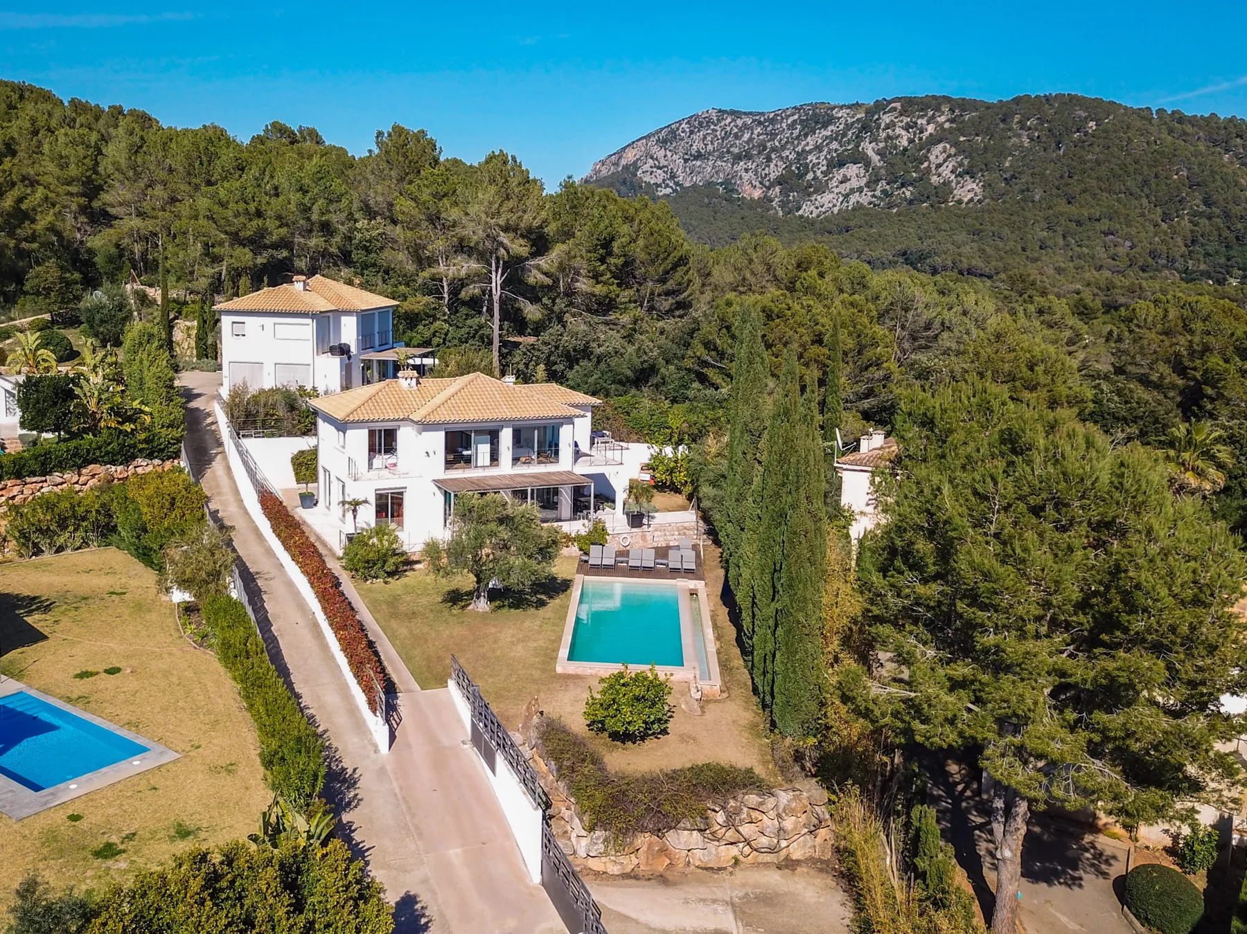 Aerial view of a house with a turquoise pool, surrounded by trees and hills.