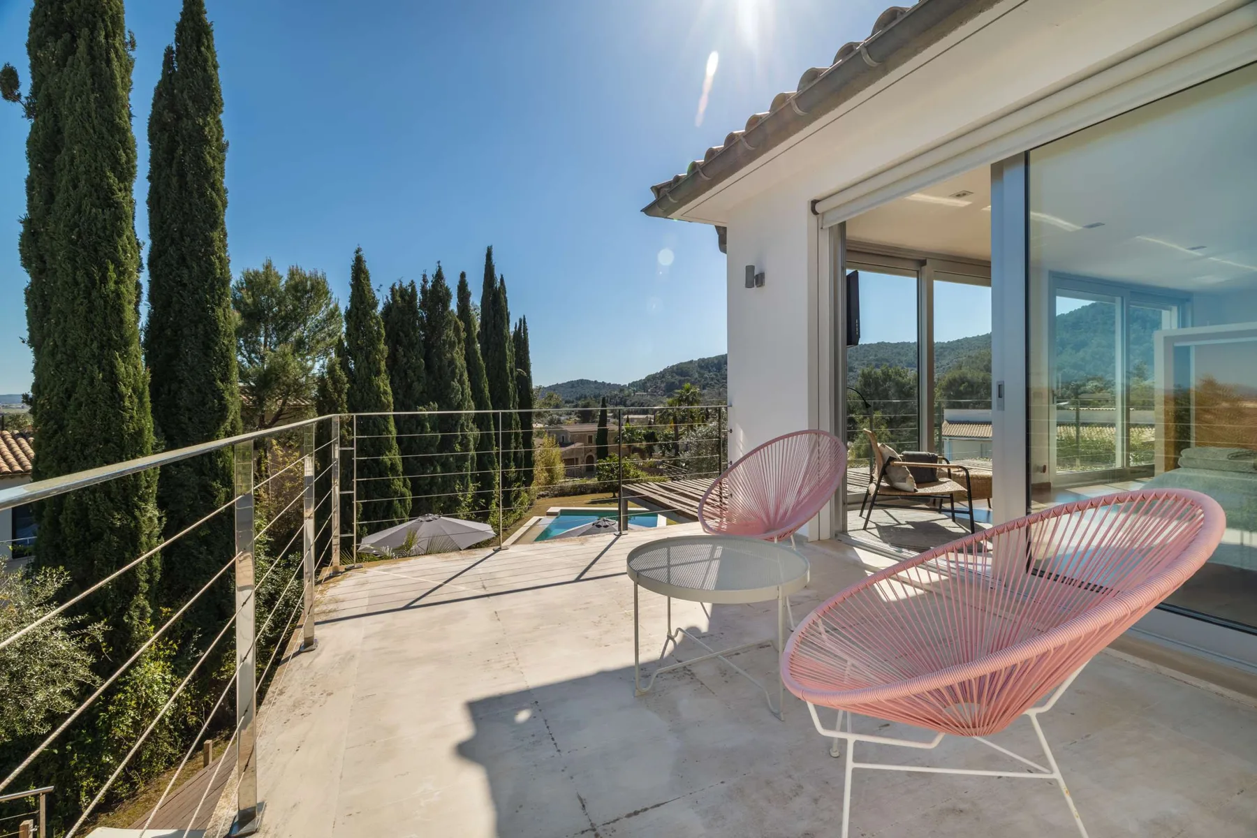 A sunlit terrace with pink seating overlooks trees and distant hills.
