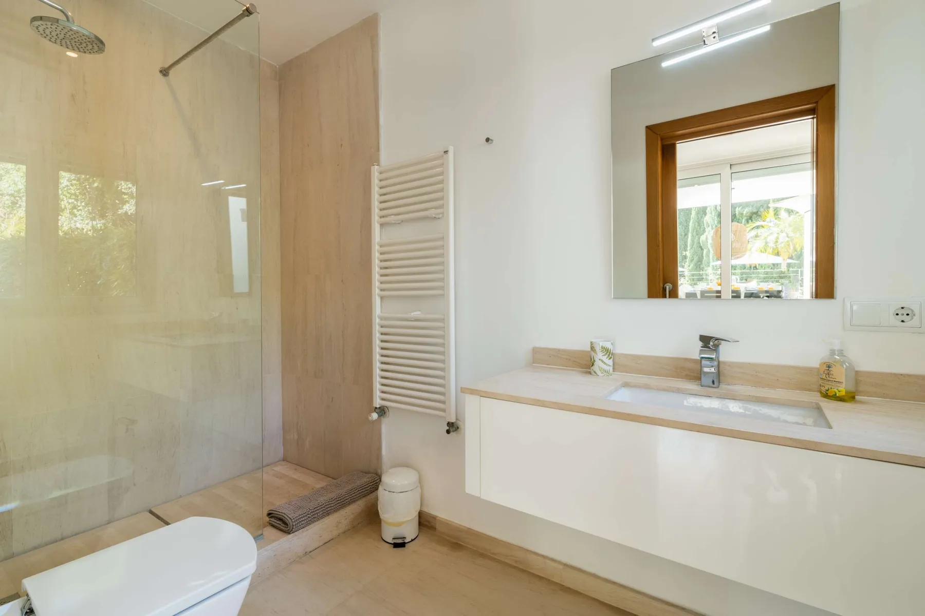 A bright bathroom with a glass shower, bathtub, and wide vanity.