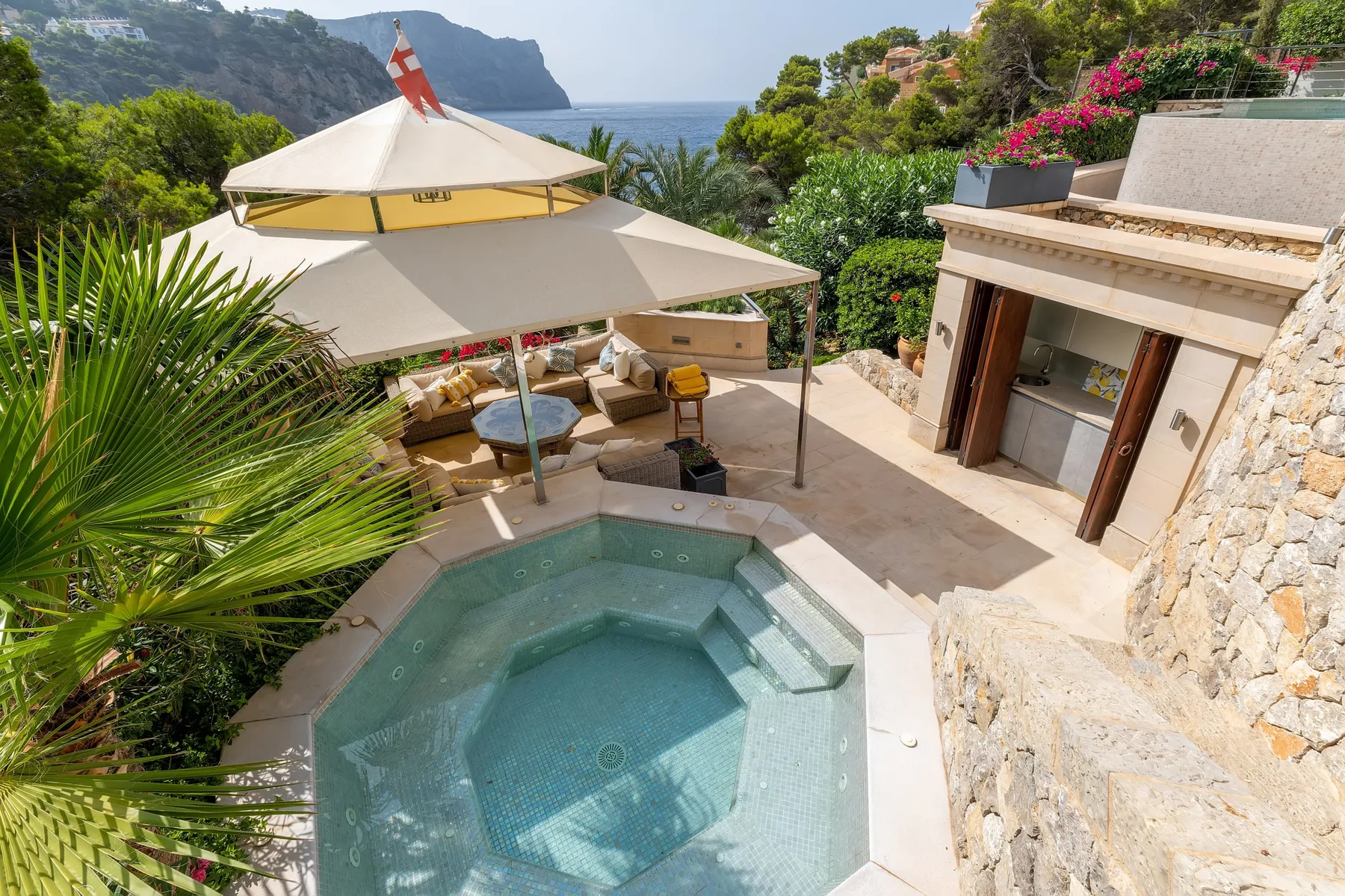 An outdoor terrace with a small pool, shaded seating, and a view of the sea.