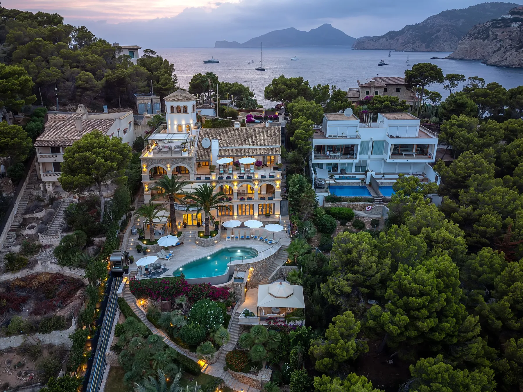 A coastal resort complex with buildings, a swimming pool, and a bay beyond.