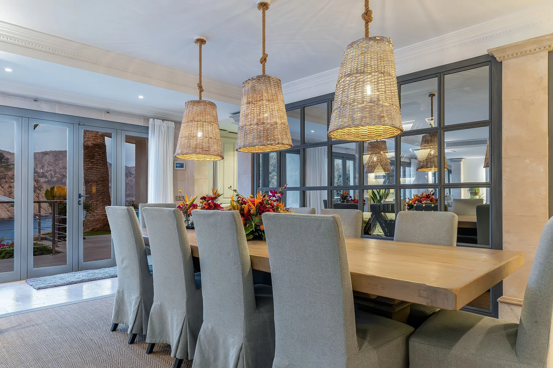 A dining area with a long table, upholstered seating, and pendant lights.