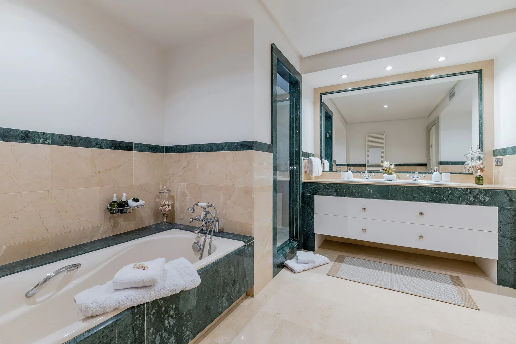 A bathroom with a bathtub and a wide vanity beneath a large mirror.