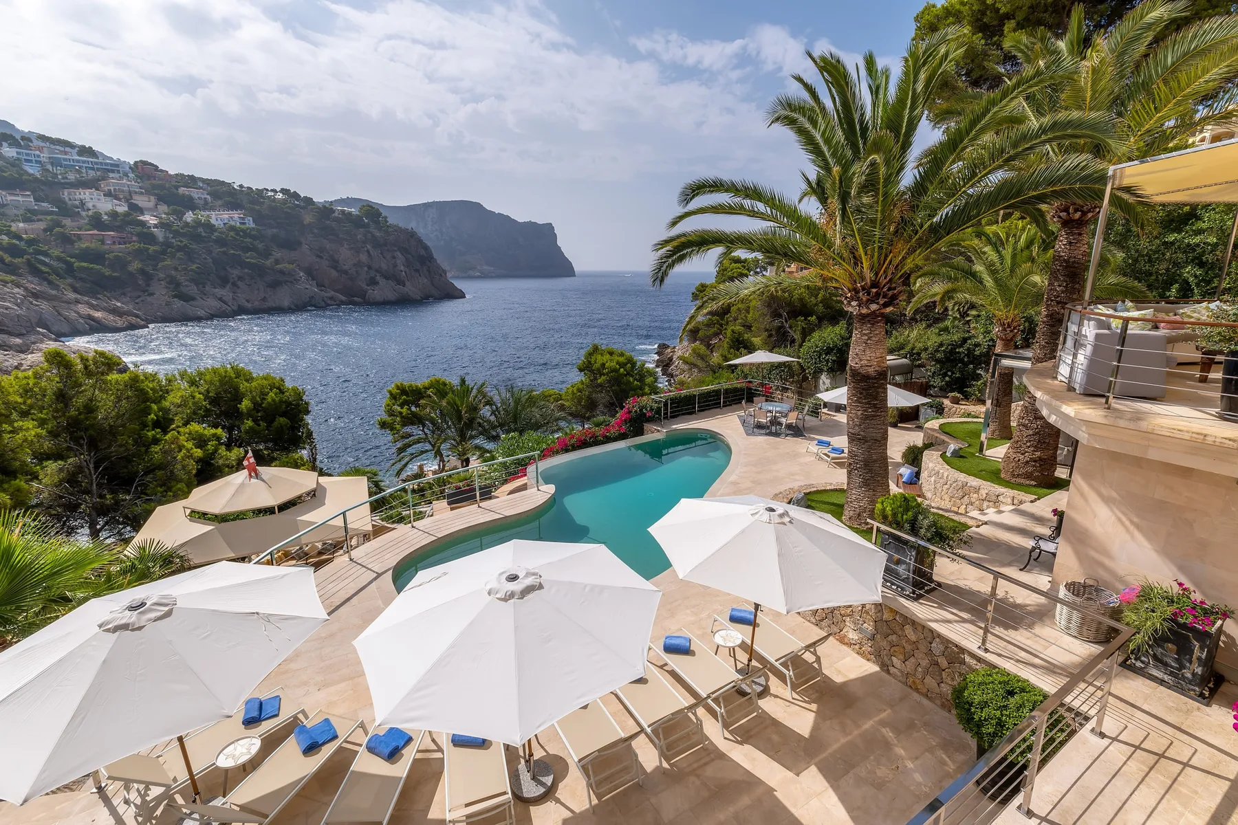 A seaside pool terrace with white umbrellas overlooks the ocean.