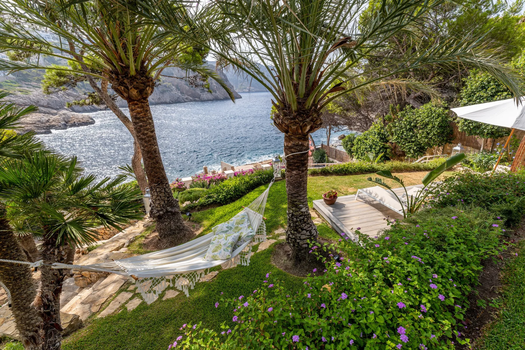 A landscaped seaside garden with palm trees, a hammock, and the water beyond.