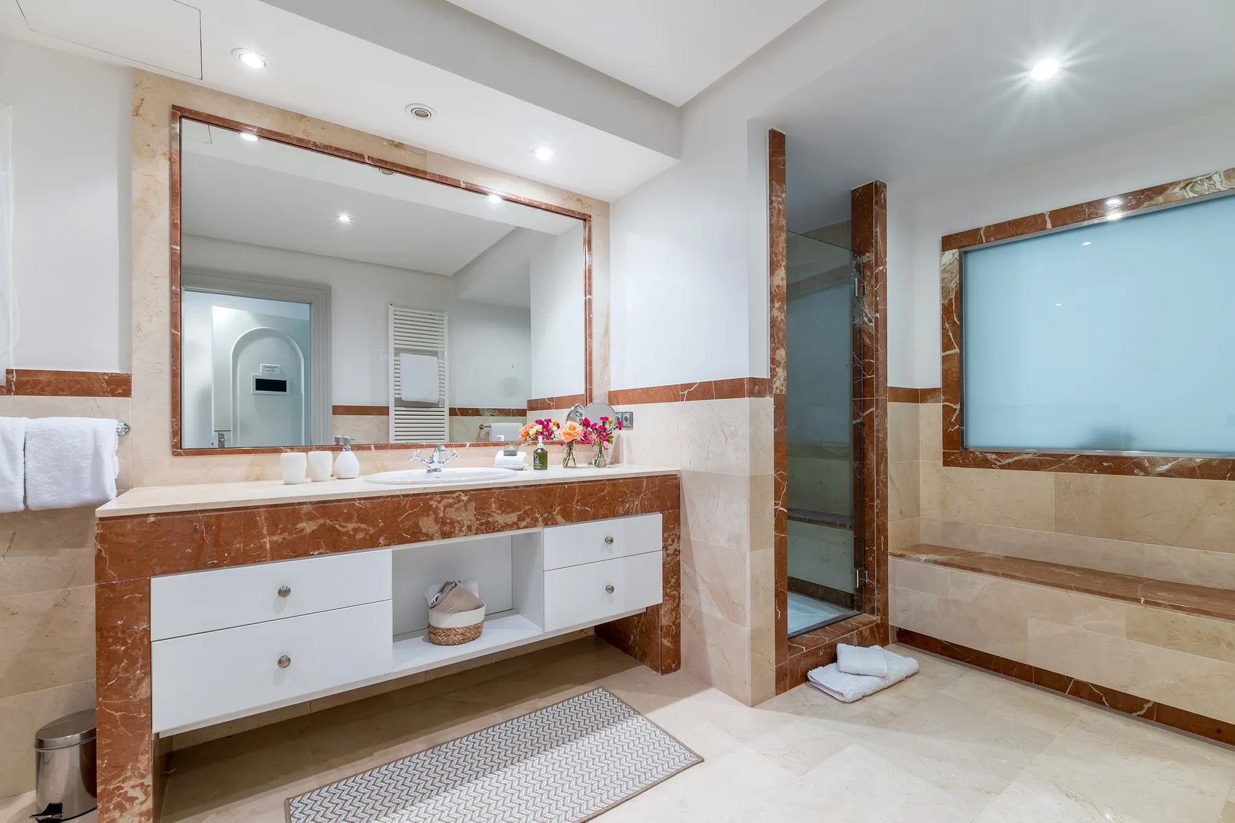 A bright bathroom with a long vanity, large mirror, and glass shower.