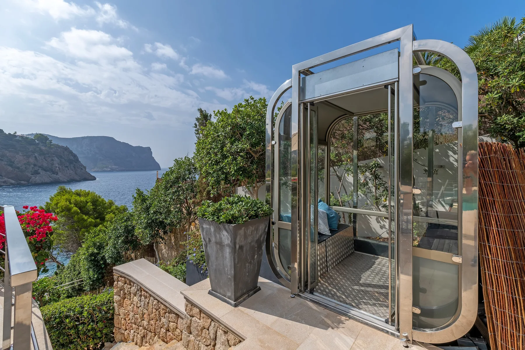 A glass-enclosed seating area opens onto a garden overlooking the sea.