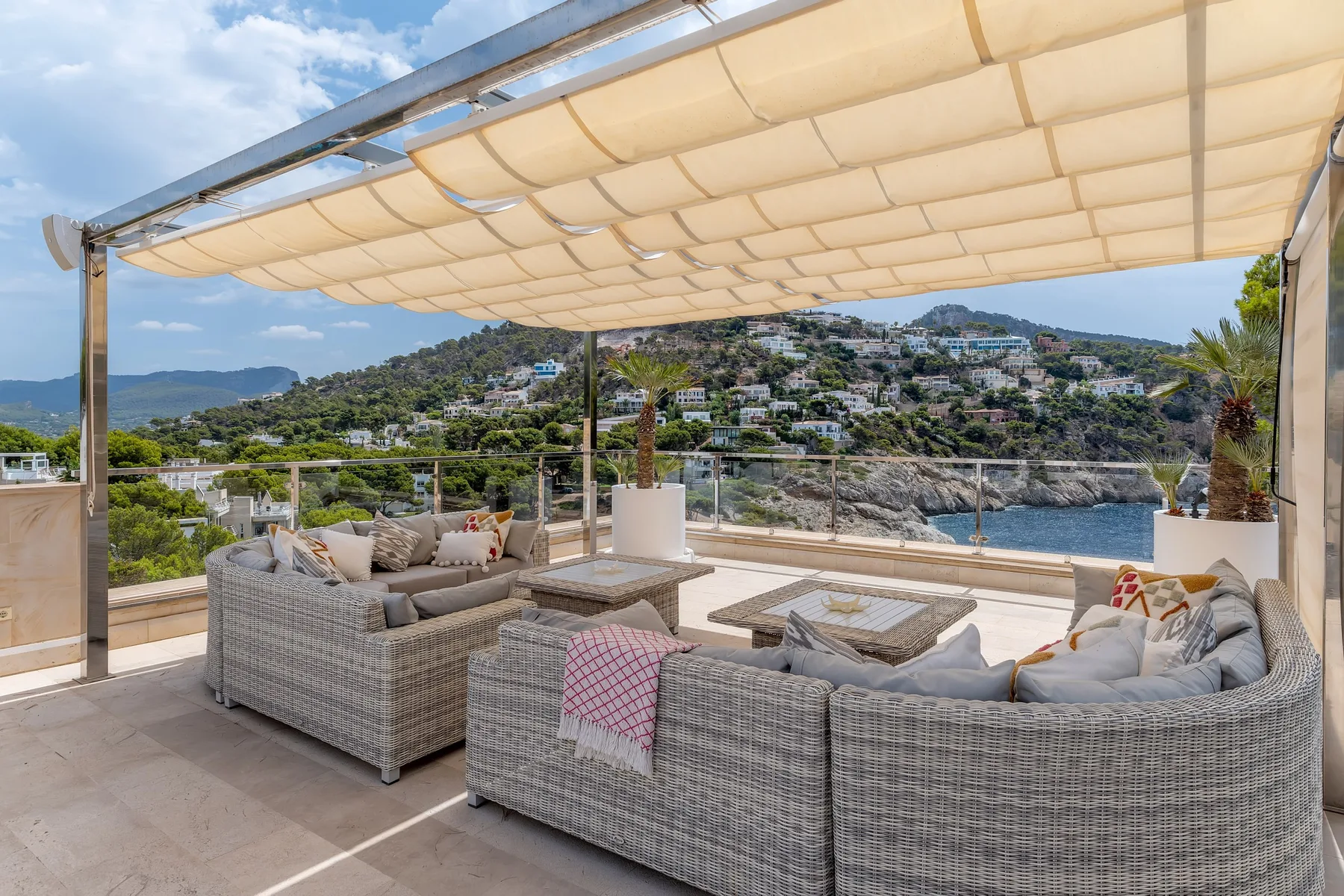 An outdoor terrace with cushioned seating and a view of the water and hills.