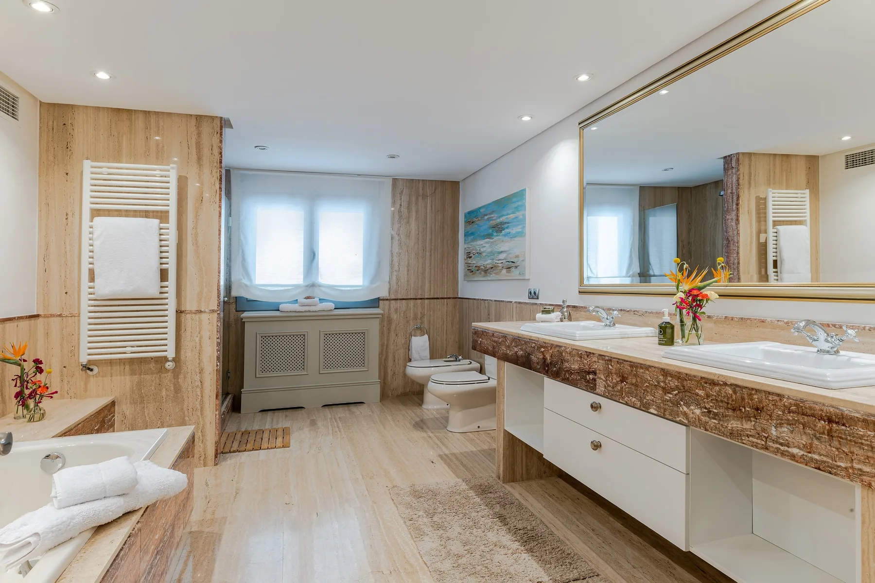 A bright bathroom with a long vanity, large mirror, and bathtub.