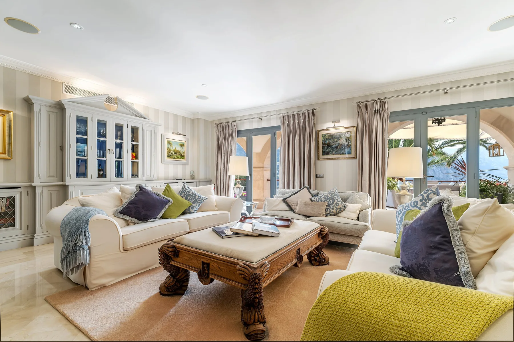 A bright living room with sofas, a wooden coffee table, and large windows.
