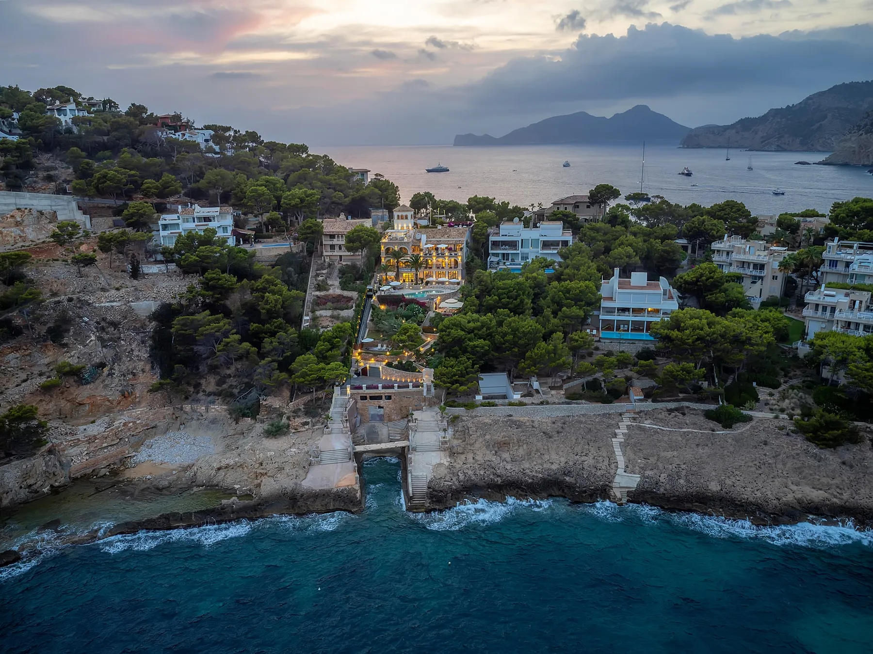 A coastal resort among trees overlooks the sea beneath a cloudy sunset sky.
