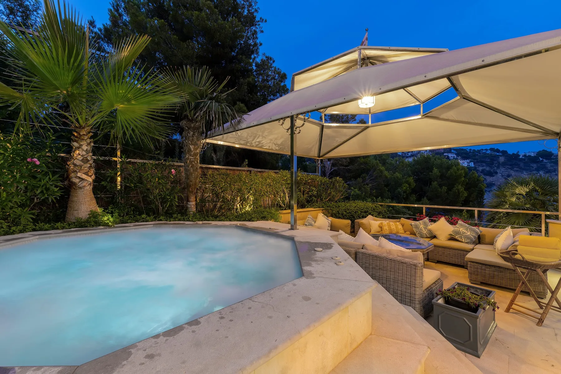 An outdoor pool beside a cushioned seating area under a canopy.