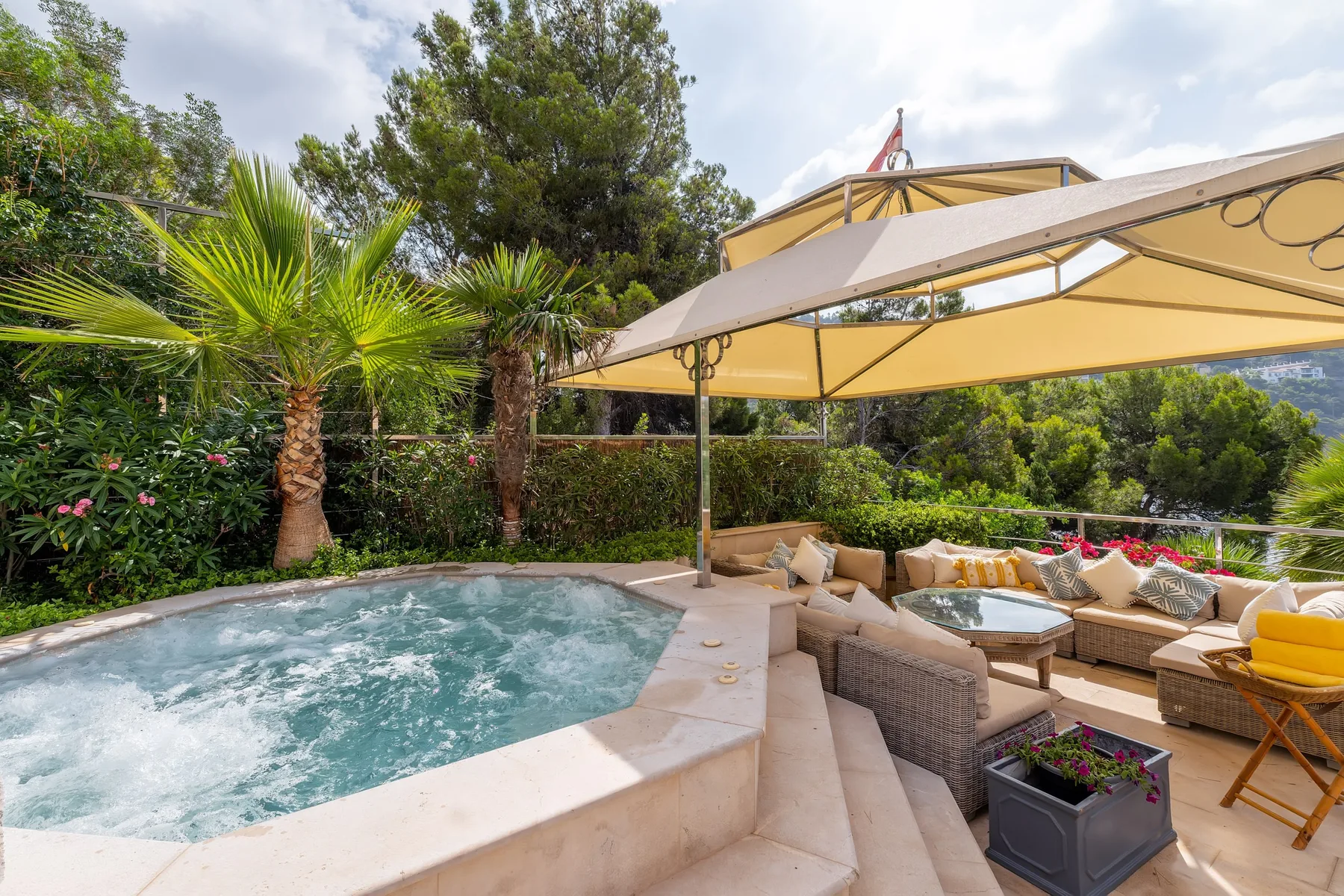An outdoor patio features a bubbling hot tub and cushioned seating beneath a large canopy.