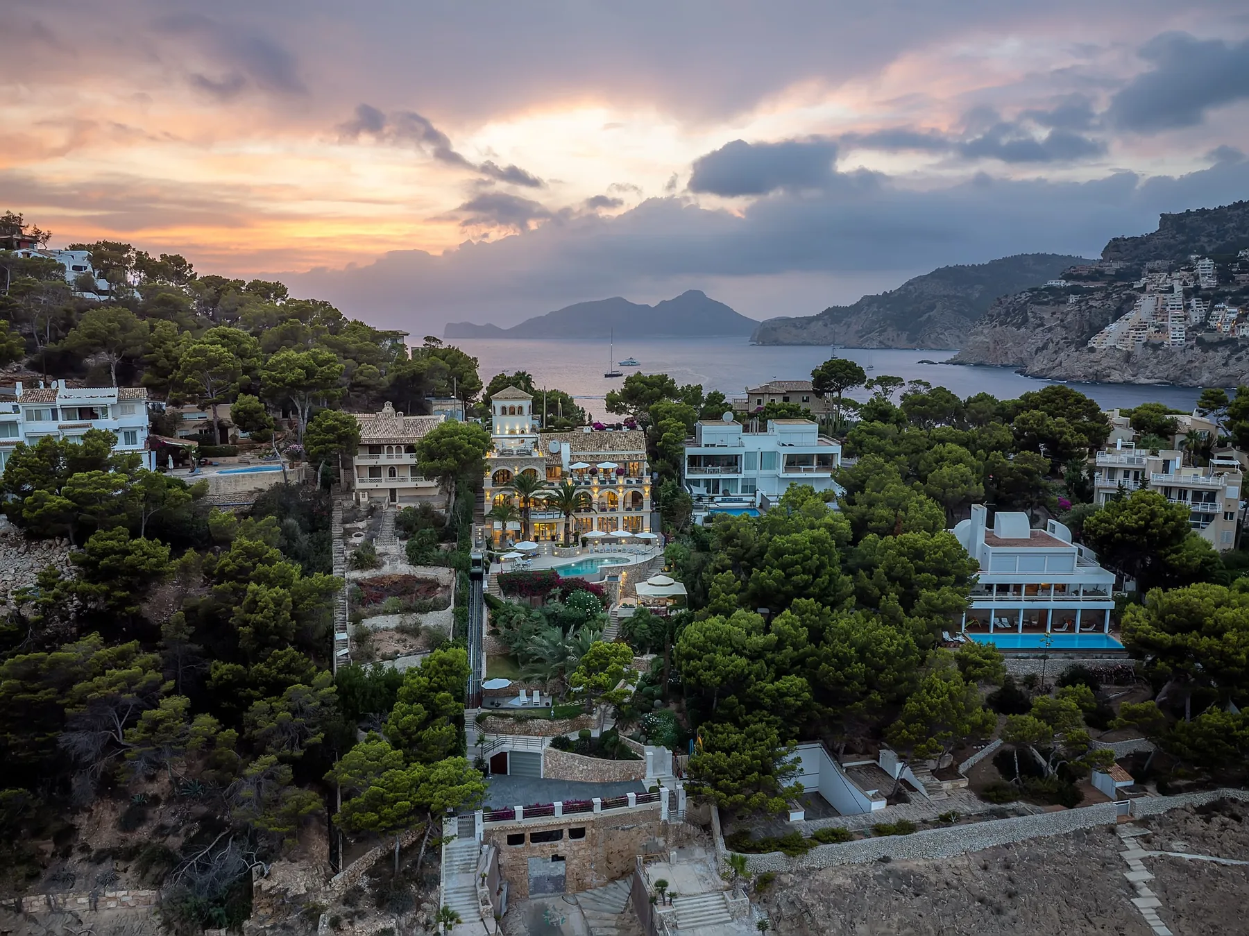 Coastal hillside homes overlook a bay beneath a colorful sunset sky.