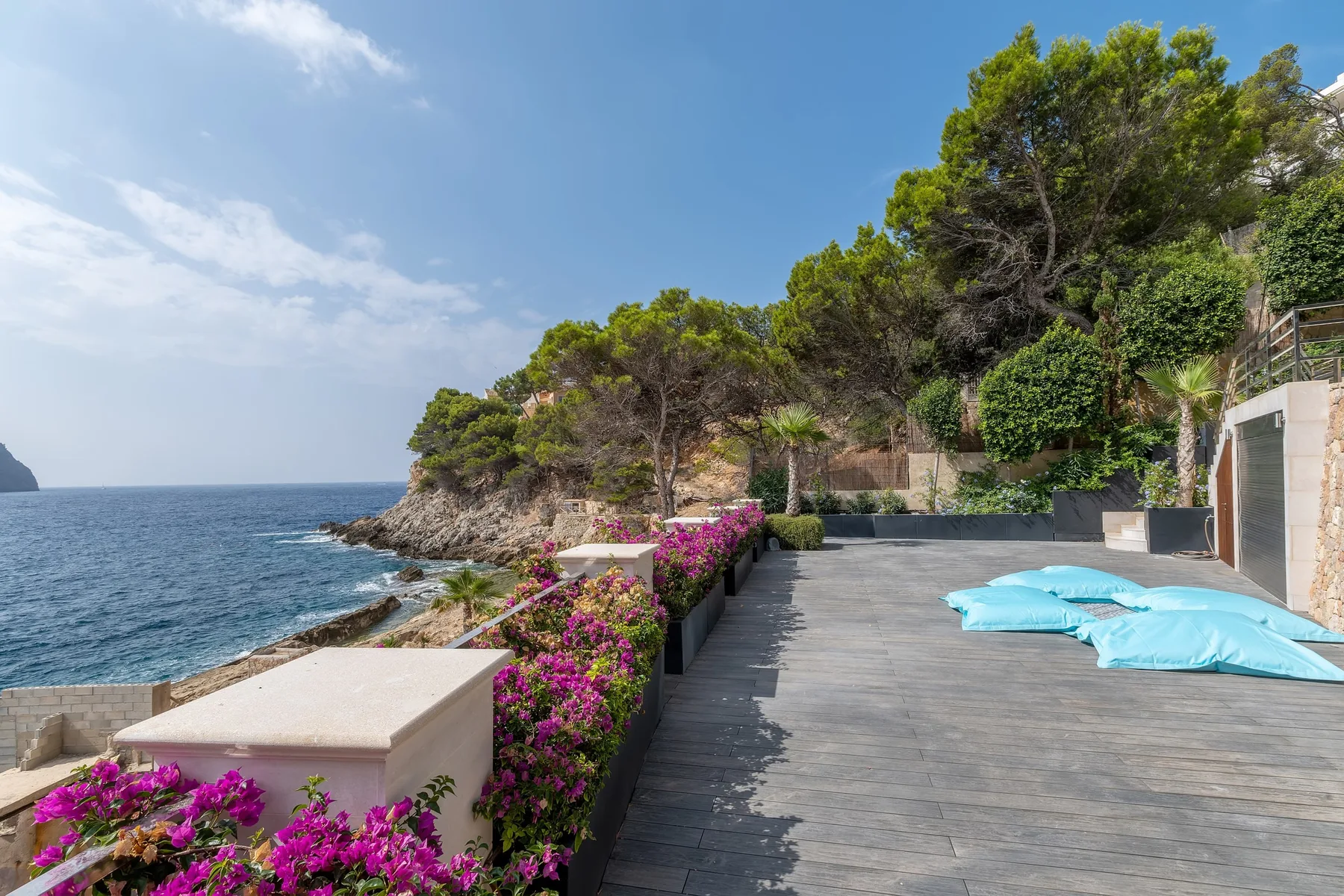 A seaside terrace with flowering plants, shaded seating, and the ocean beyond.
