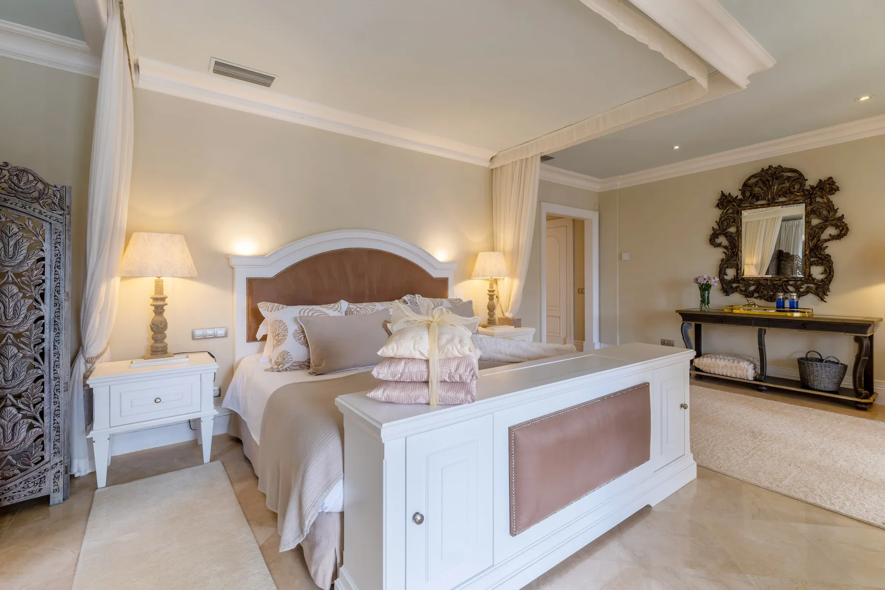 A bedroom with a large bed, bedside tables, and a decorative mirror.