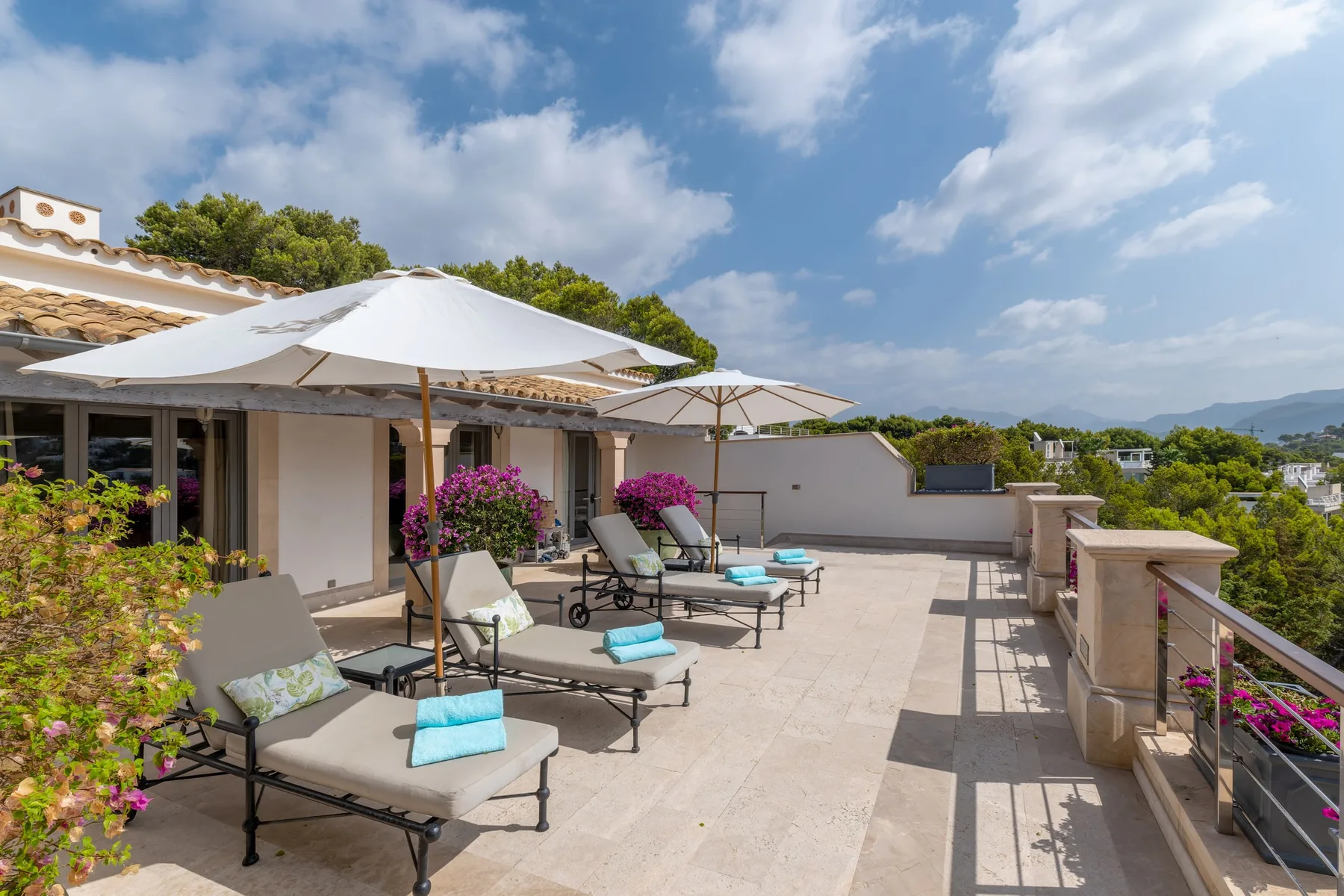 A rooftop terrace with lounge seating, umbrellas, and potted flowers.