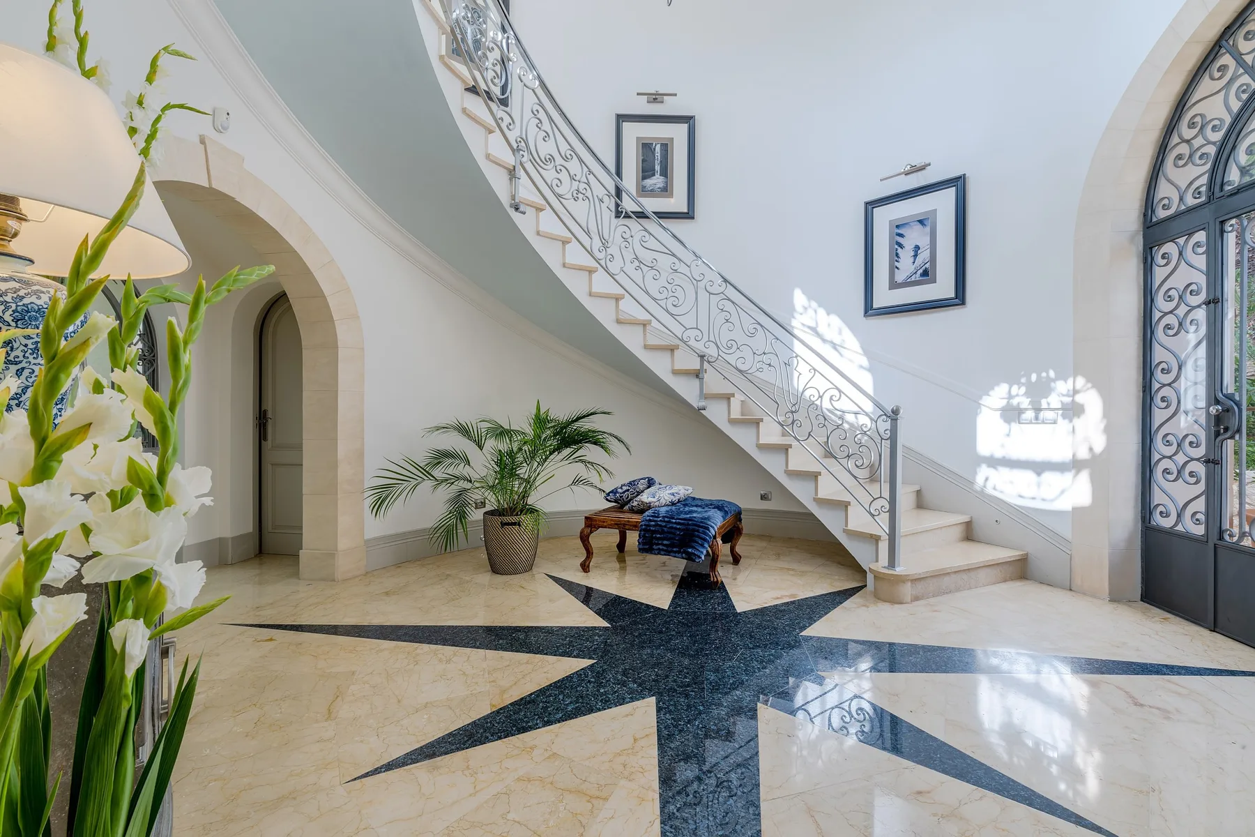 A grand entry hall features a curved staircase and patterned stone flooring.