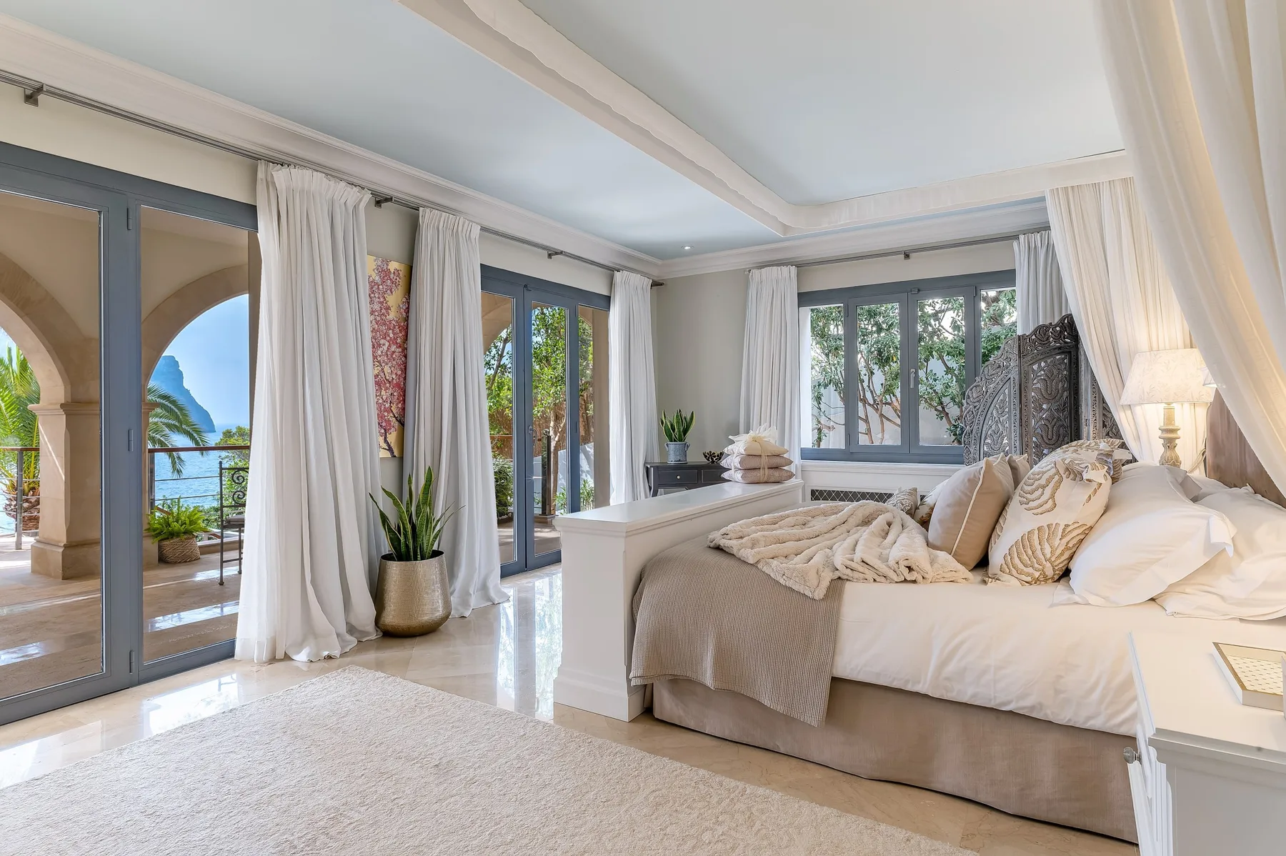 A bright bedroom with a large bed beside windows and glass doors.