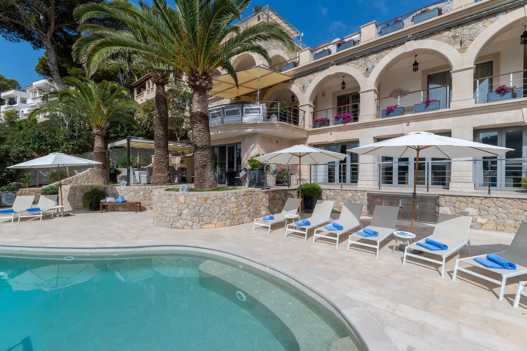 An outdoor swimming pool sits beside a patio with loungers and umbrellas.