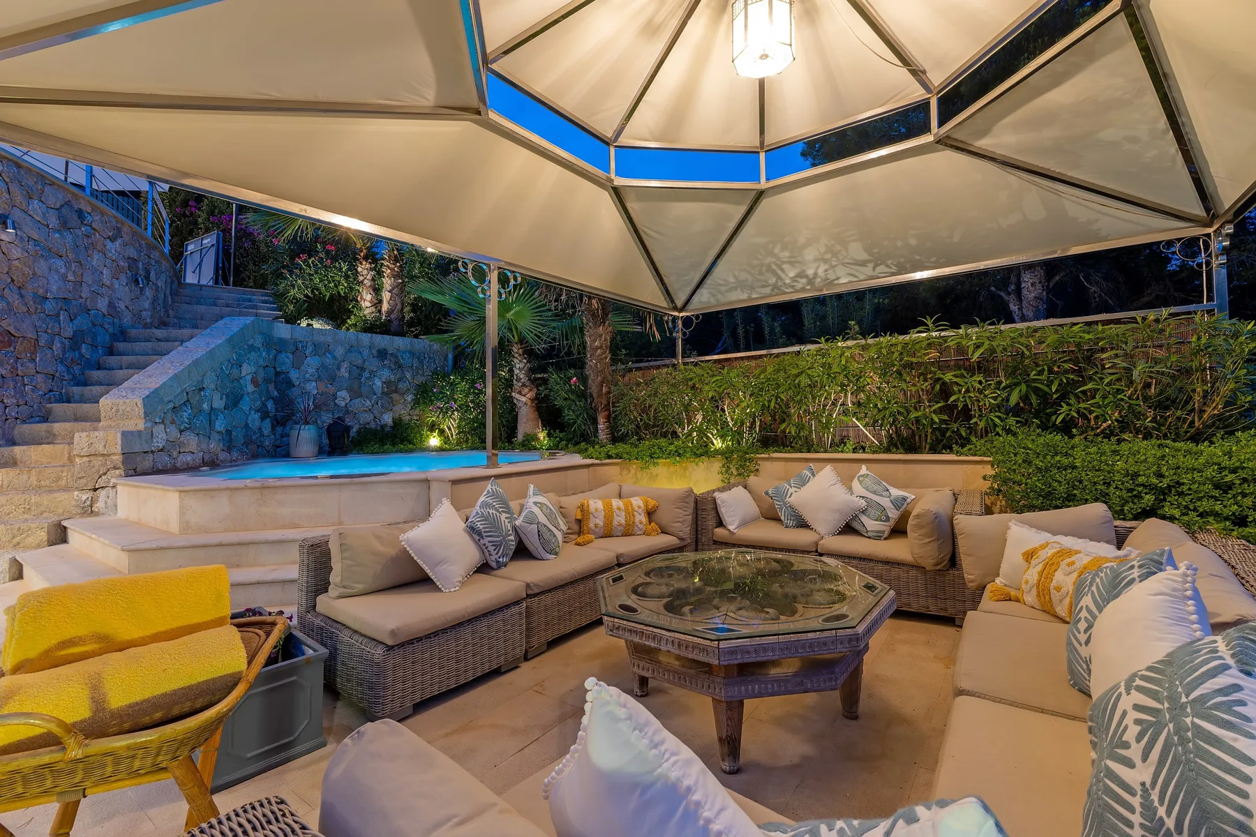 An outdoor lounge with cushioned seating around a low table beside a pool.