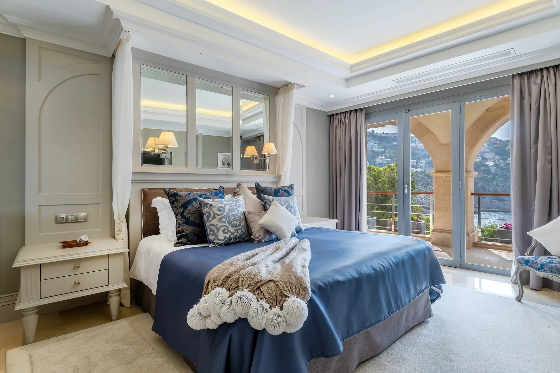 A bedroom with a blue-covered bed beside glass doors opening onto a balcony.