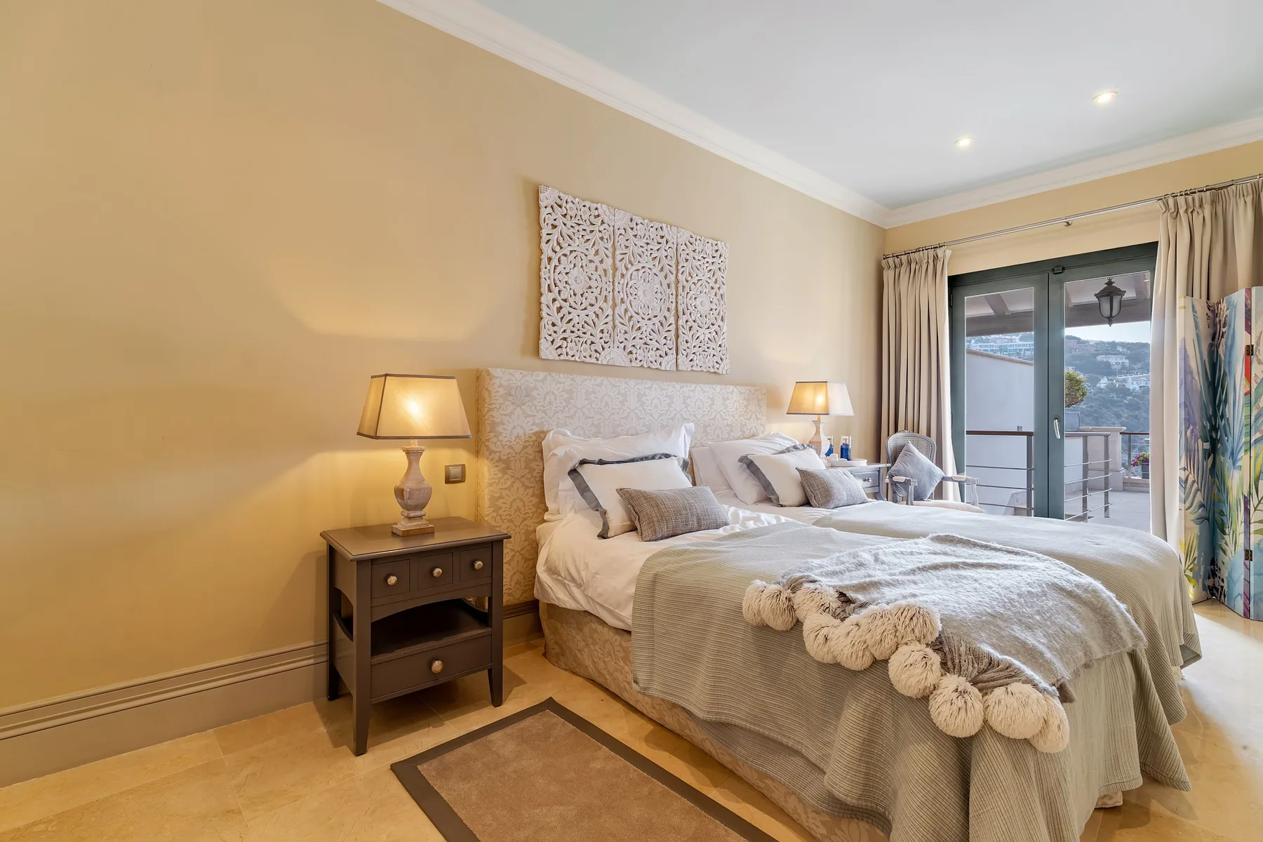A bedroom with a large bed, bedside tables, and curtains by the glass doors.