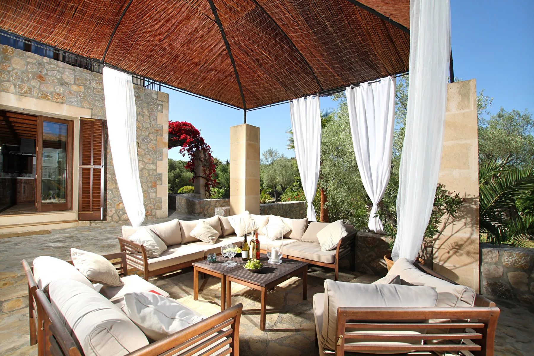 An outdoor lounge beneath a woven canopy, with cushioned seating and a low table.