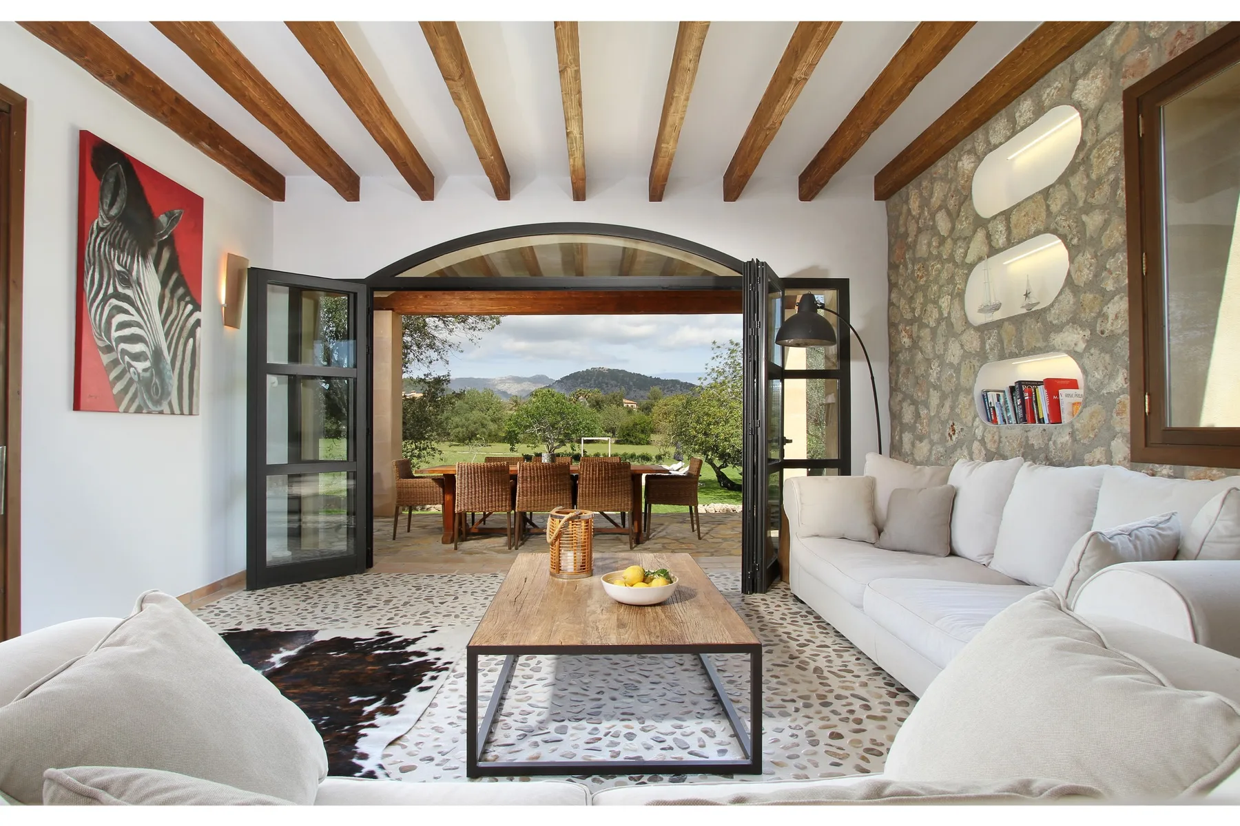 A bright living room opens through wide doors to an outdoor dining area and garden.