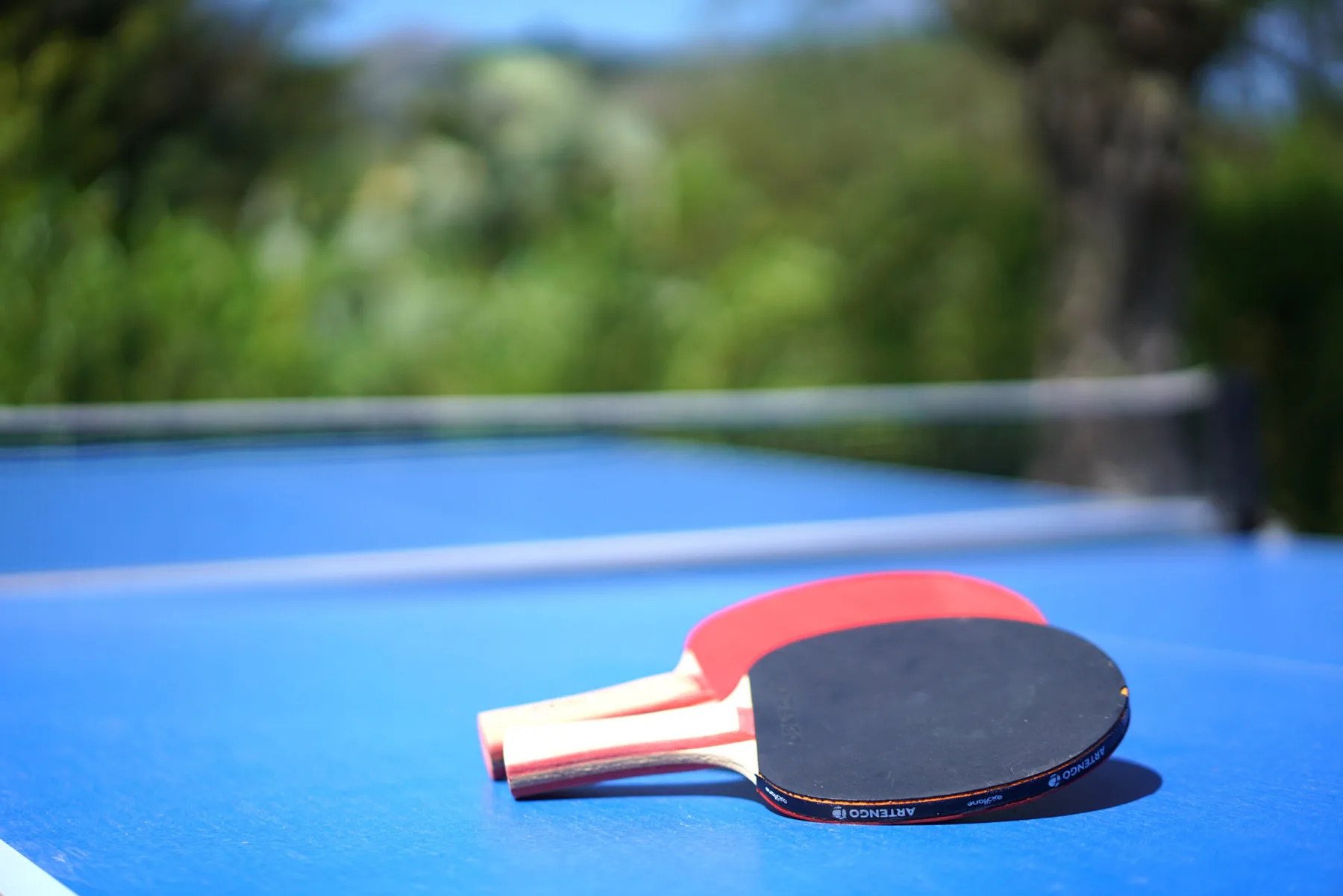 A table tennis paddle rests on a blue table outdoors.