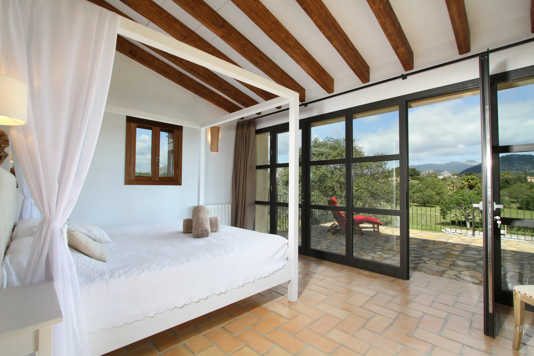 A bedroom with a white bed beside glass doors opening onto a patio.