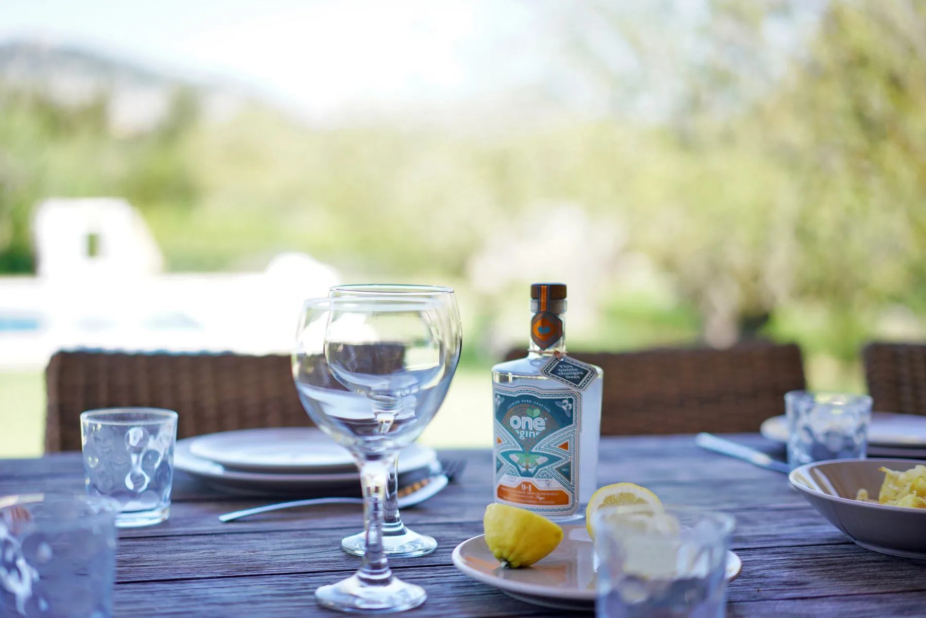 An outdoor dining table is set with glasses, plates, and a bottle.