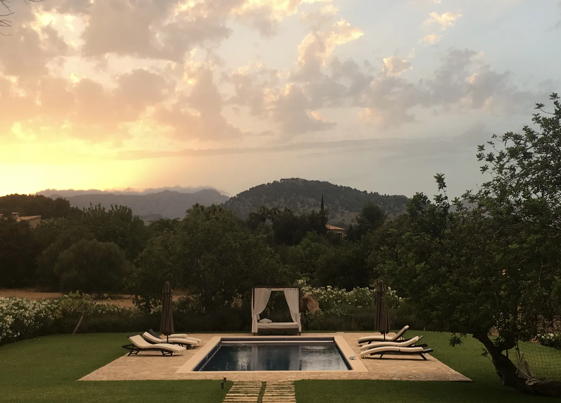 A garden pool and lounge seating overlook wooded hills beneath a sunset sky.
