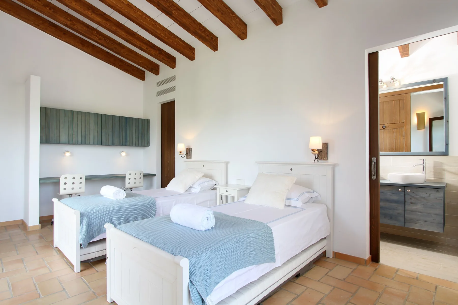 A bright bedroom with two beds dressed in pale blue and white linens.