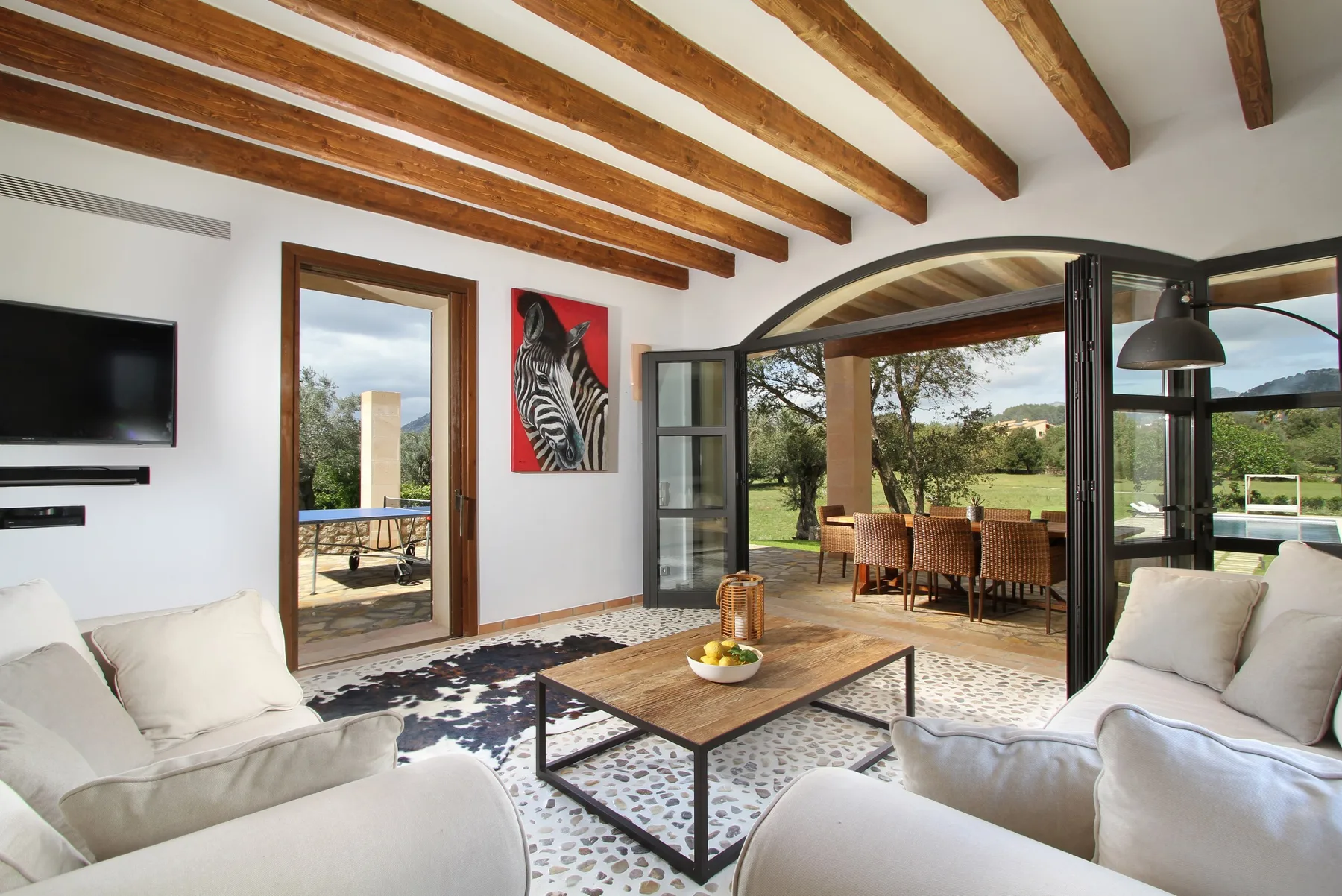 A bright living room opens onto a dining area through wide glass doors.