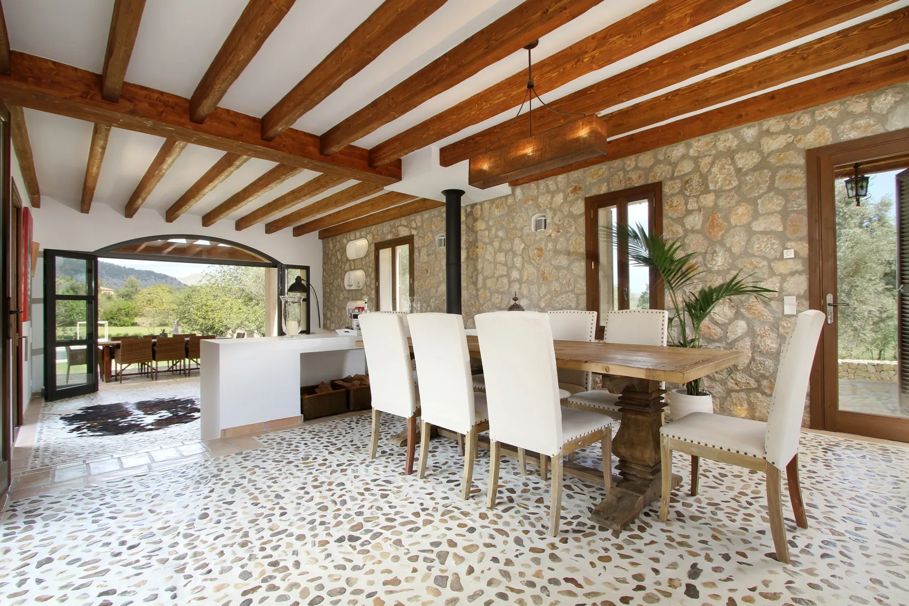 A dining area with a wooden table and white chairs beneath exposed wooden ceiling beams.
