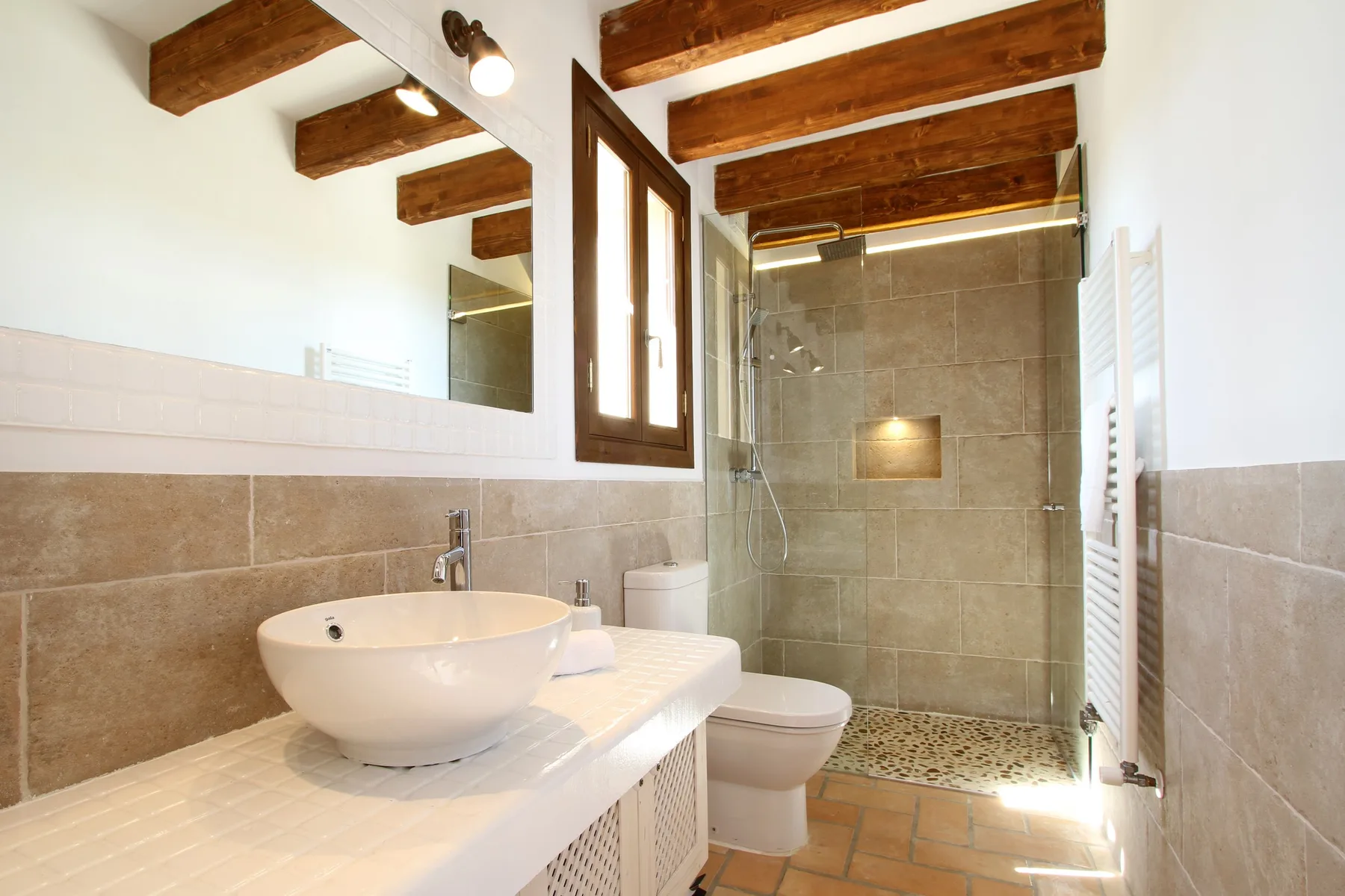A bathroom with a sink, toilet, and tiled shower area beneath exposed wooden beams.