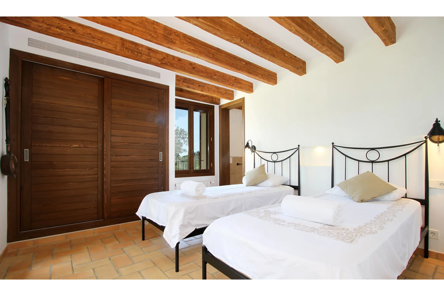A bright bedroom with two beds, wooden ceiling beams, and a window.