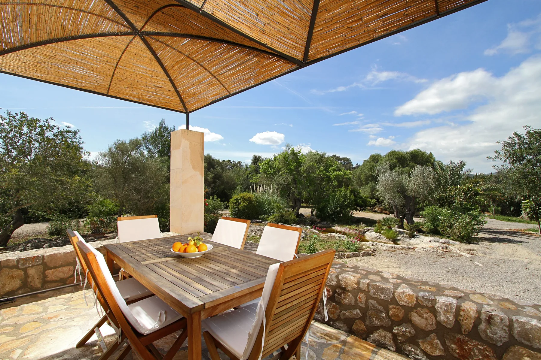 An outdoor dining area with a wooden table beneath a woven shade canopy.