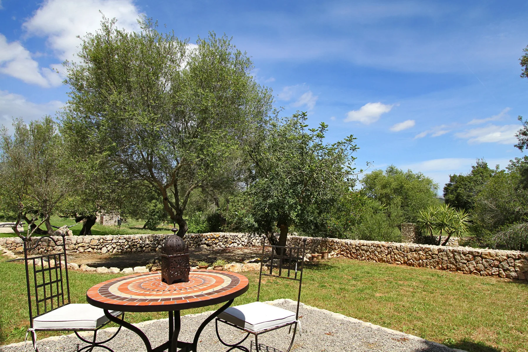 An outdoor patio has a round table and chairs beside a stone garden wall.
