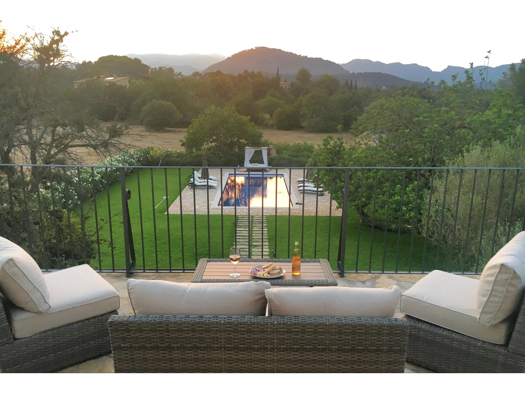 A patio seating area overlooks a lawn, swimming pool, and tree-covered hills.