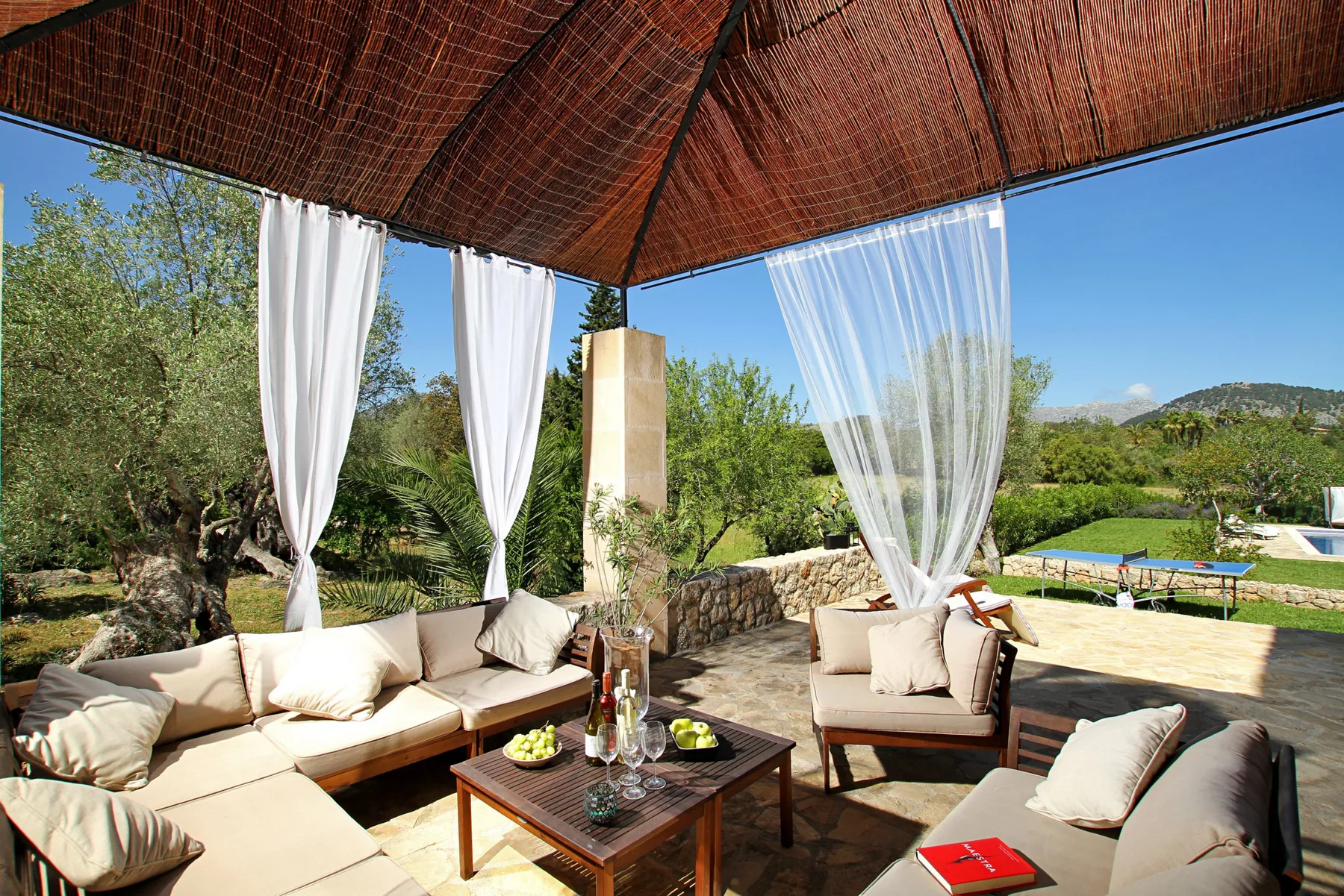 An outdoor patio seating area under a woven canopy overlooks green hills.