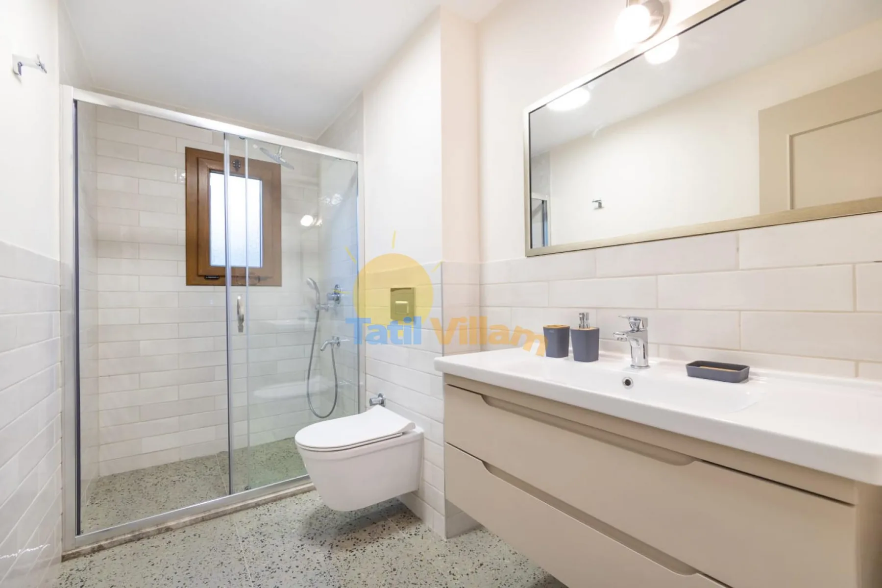 A bright bathroom with a glass shower, toilet, and long vanity.
