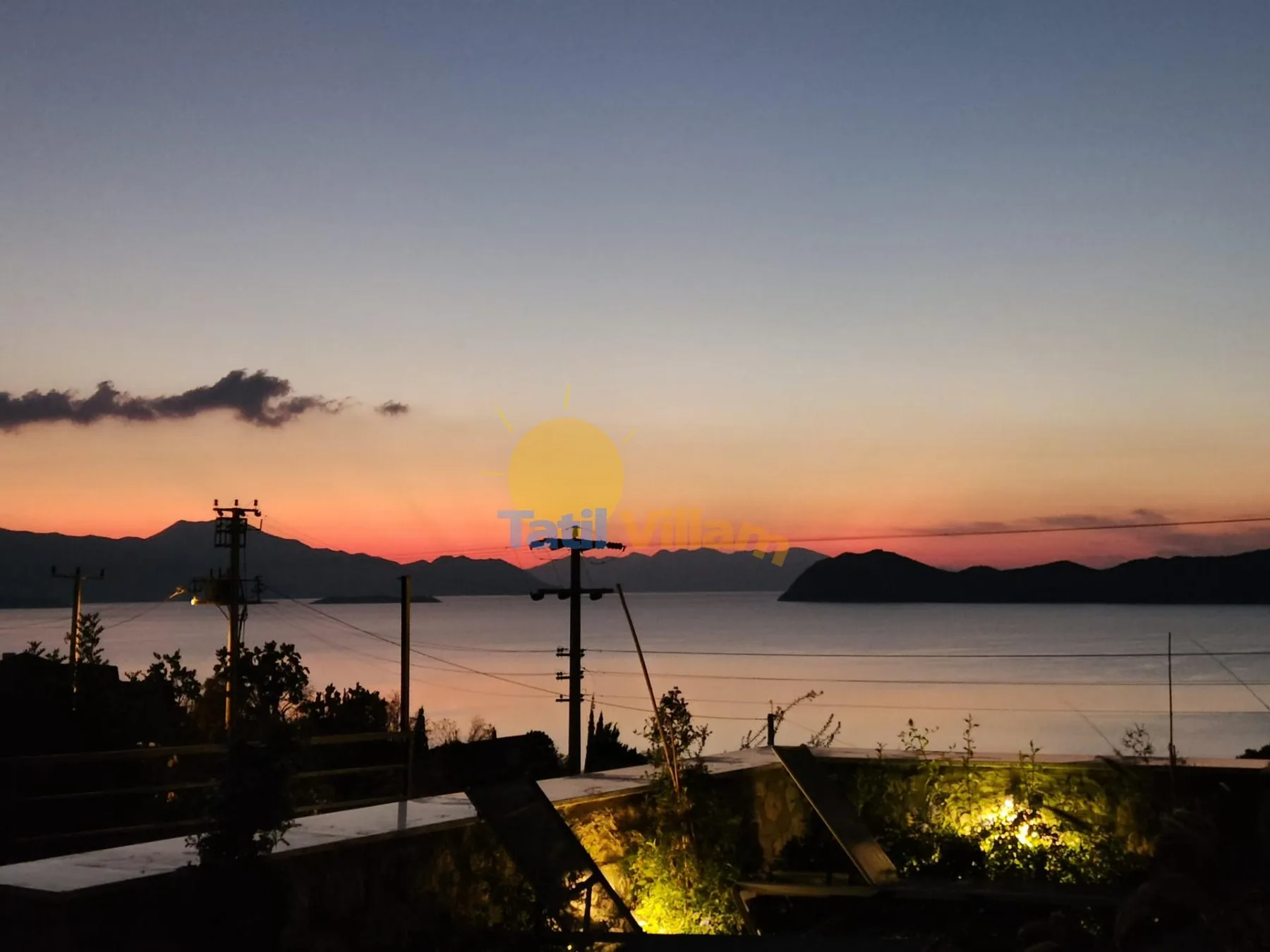 Sunset over a calm bay, with dark hills along the horizon.