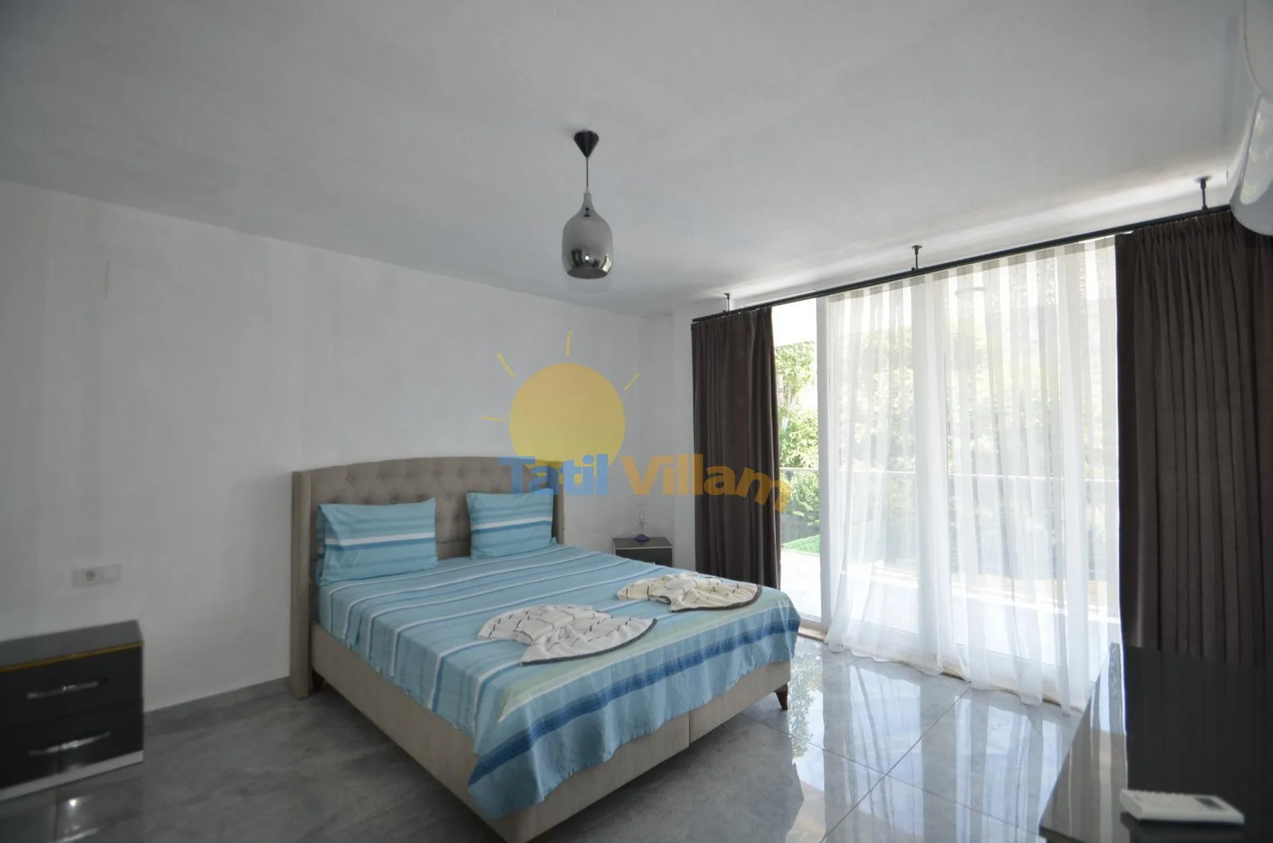 Un dormitorio con una cama de rayas azules junto a grandes ventanas con cortinas.