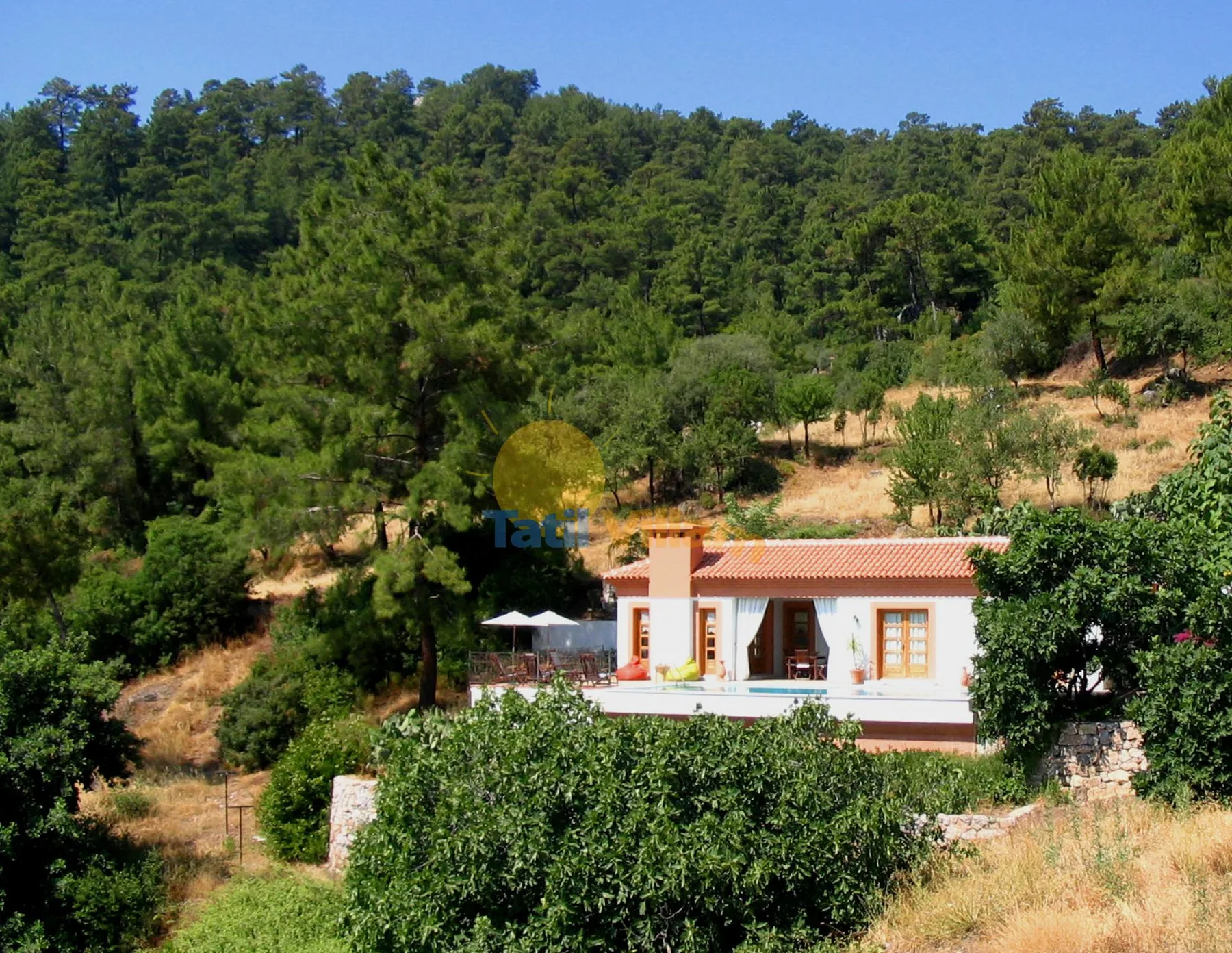 Una casa blanca con tejado de terracota se encuentra entre árboles en una ladera.