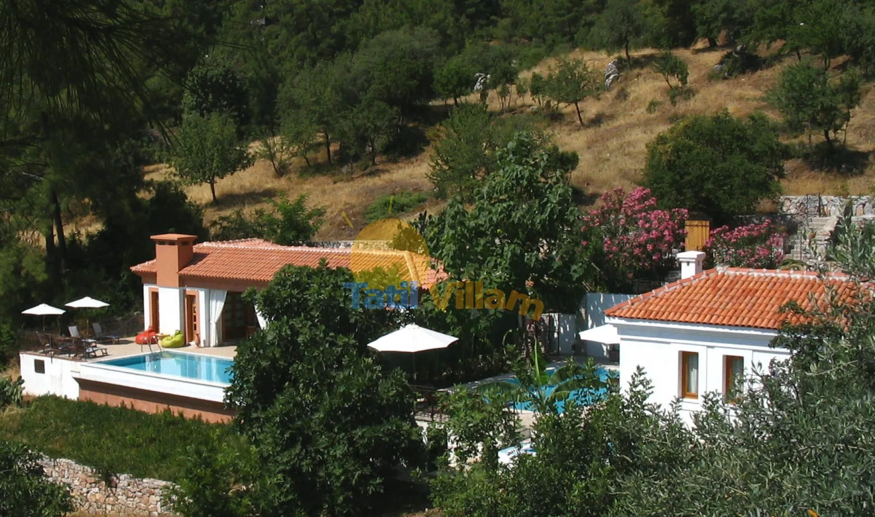 Una propiedad en la ladera con dos edificios blancos, techos de terracota y una piscina.