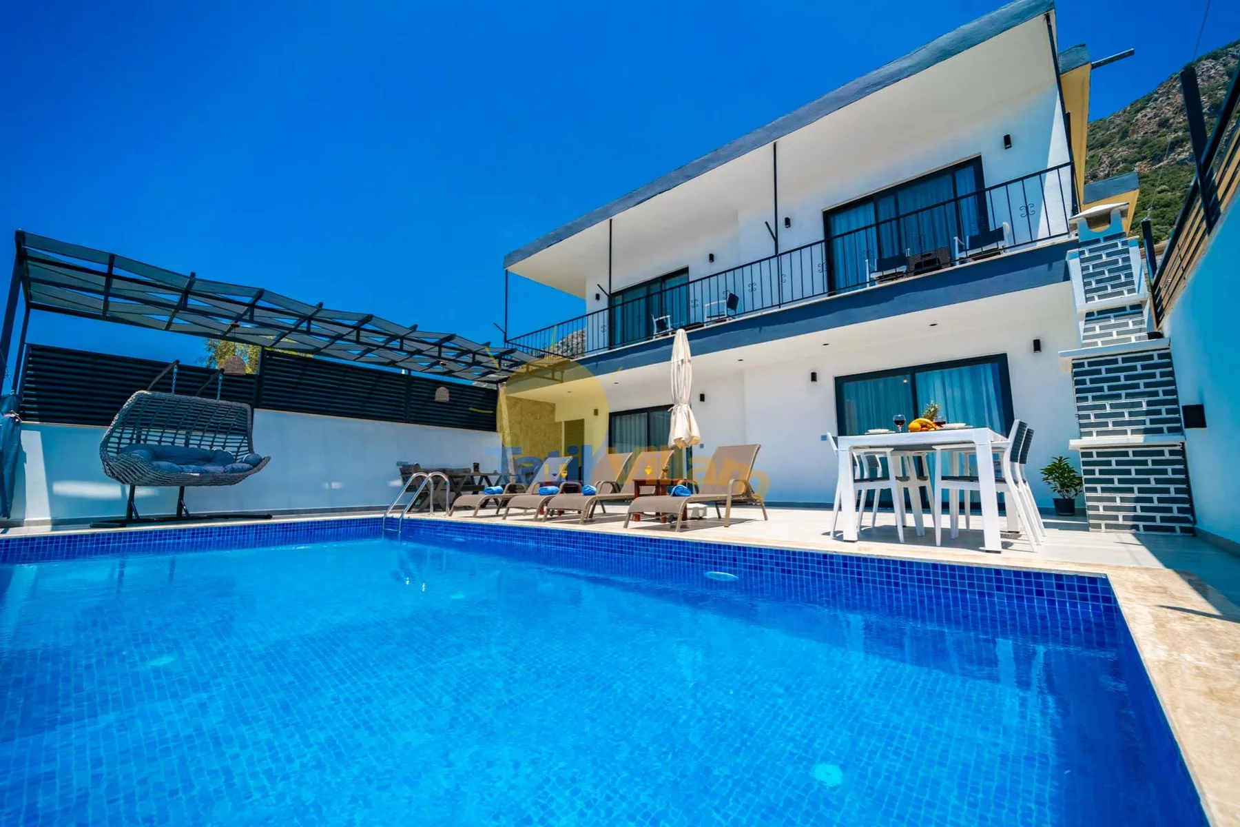 An outdoor swimming pool beside a modern white building with patio seating.